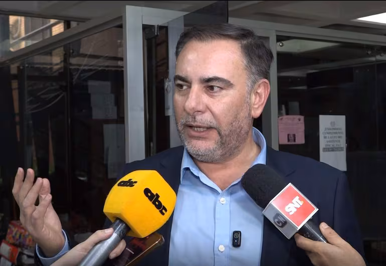 El senador Ever Villalba, con camisa azul y saco oscuro, gesticula mientras habla a reporteros en un ambiente urbano.